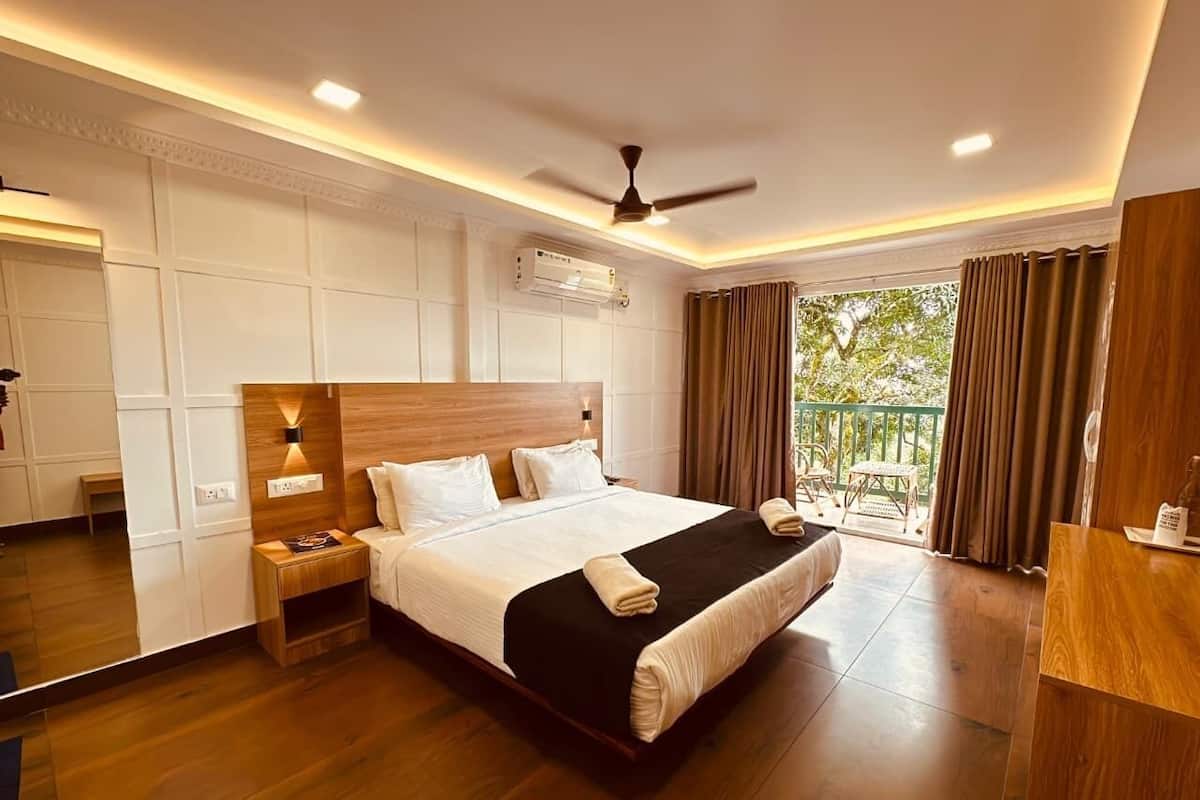 A hotel room with a large bed, bedside tables, a ceiling fan, an air conditioning unit, and a balcony with curtains.