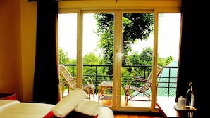 A hotel room with a bed, a balcony with wicker chairs, and a view of greenery outside. - Bella Vista Resort (Devikolam)