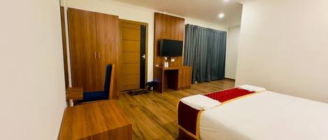 A hotel room with a bed, a desk, a wardrobe, a television, and a ceiling fan.