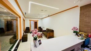 A reception area with a white reception desk, seating area with sofas, a potted plant, and a wall-mounted clock. - Bella Vista Resort (Devikolam)