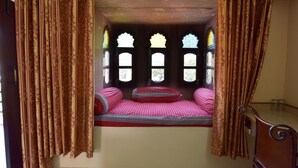 A room with a bed, curtains, and a window with decorative glass. - Jee Ri Haveli (Jodhpur)