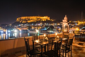 Une terrasse avec des tables et des chaises donnant sur un paysage urbain, avec un bâtiment imposant situé sur une colline.