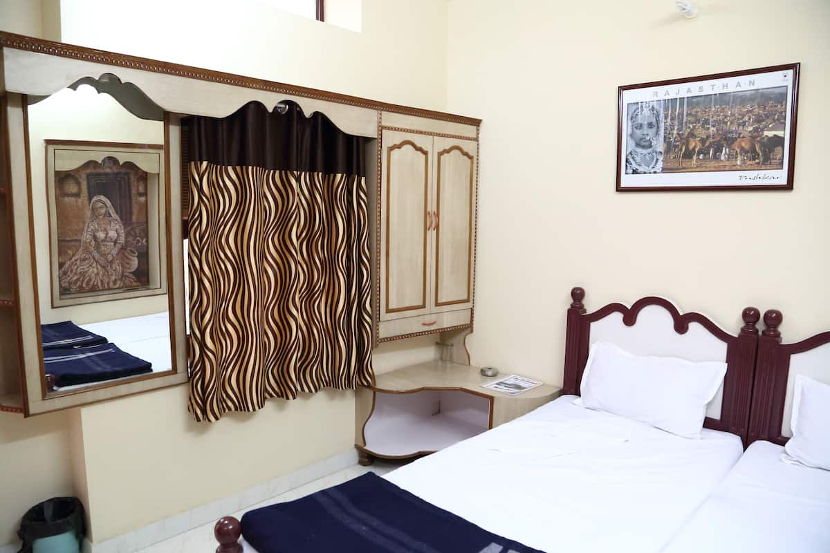 A hotel room with a bed, a wardrobe, a mirror, a framed picture of Rajasthan, and a curtain with a wavy pattern.