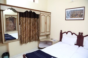 Hotelkamer met een bed, een kledingkast, een spiegel, een lijst met een afbeelding van Rajasthan, en een gordijn met een golvend patroon.