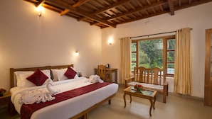 A hotel room with a large bed, wooden headboard, two bedside tables, a wooden chair, a small table with a vase of flowers, and a window with curtains. - Bracknell Forest (Udumbanchola)