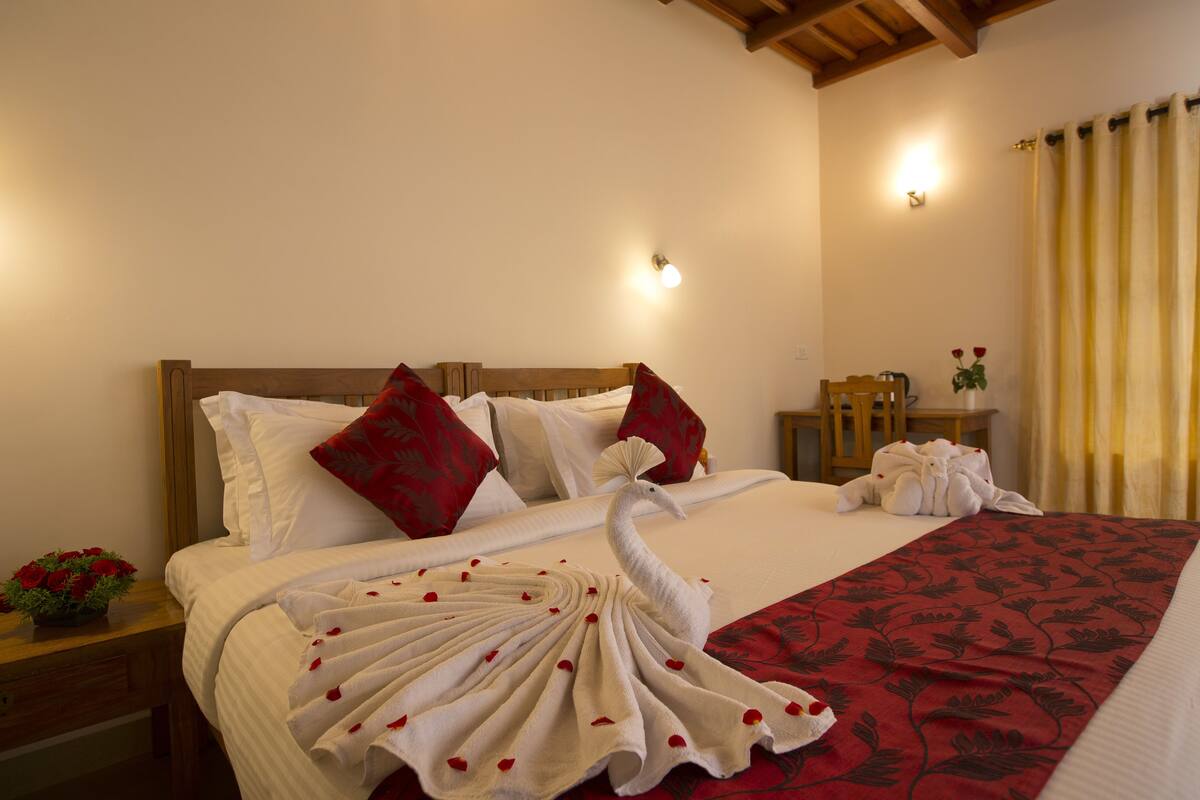 A neatly made bed with a swan towel design, red pillows, and a red and black patterned blanket.