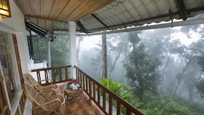 A balcony with wicker chairs and a small table, overlooking a forested area with mist. - Bracknell Forest (Udumbanchola)