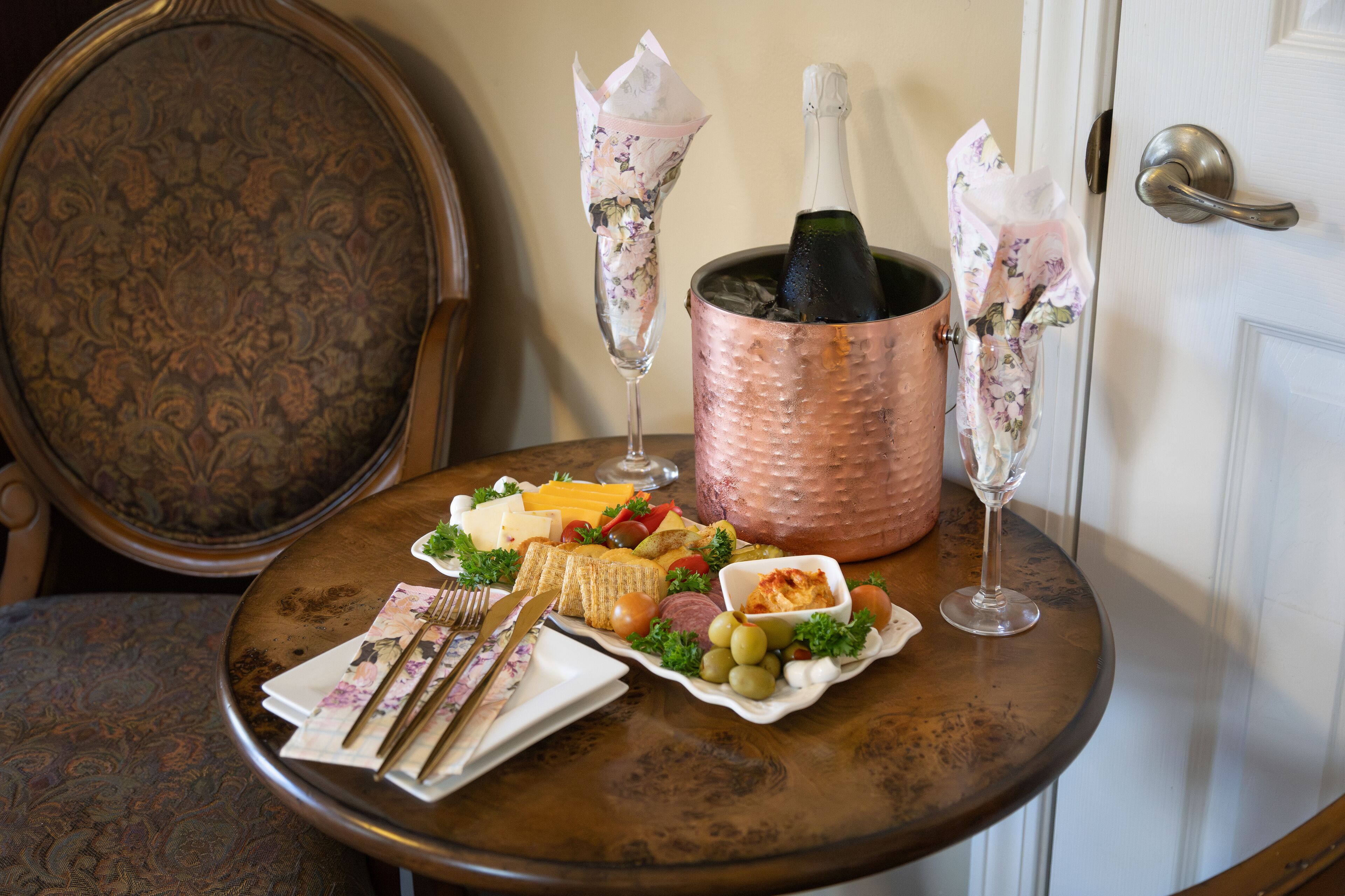 A table with a variety of food items, a bottle of champagne, and two champagne flutes.