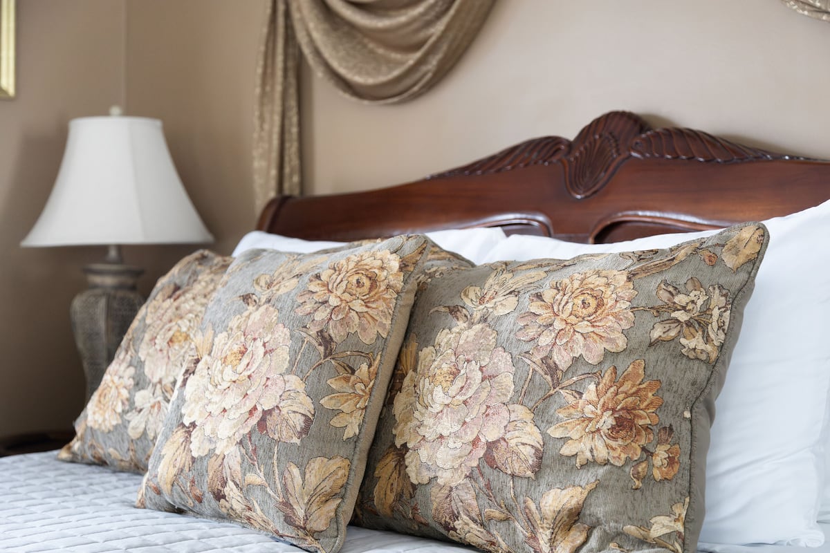 Una cama con almohadas de estampado floral, un cabecero de madera y una lámpara de noche.