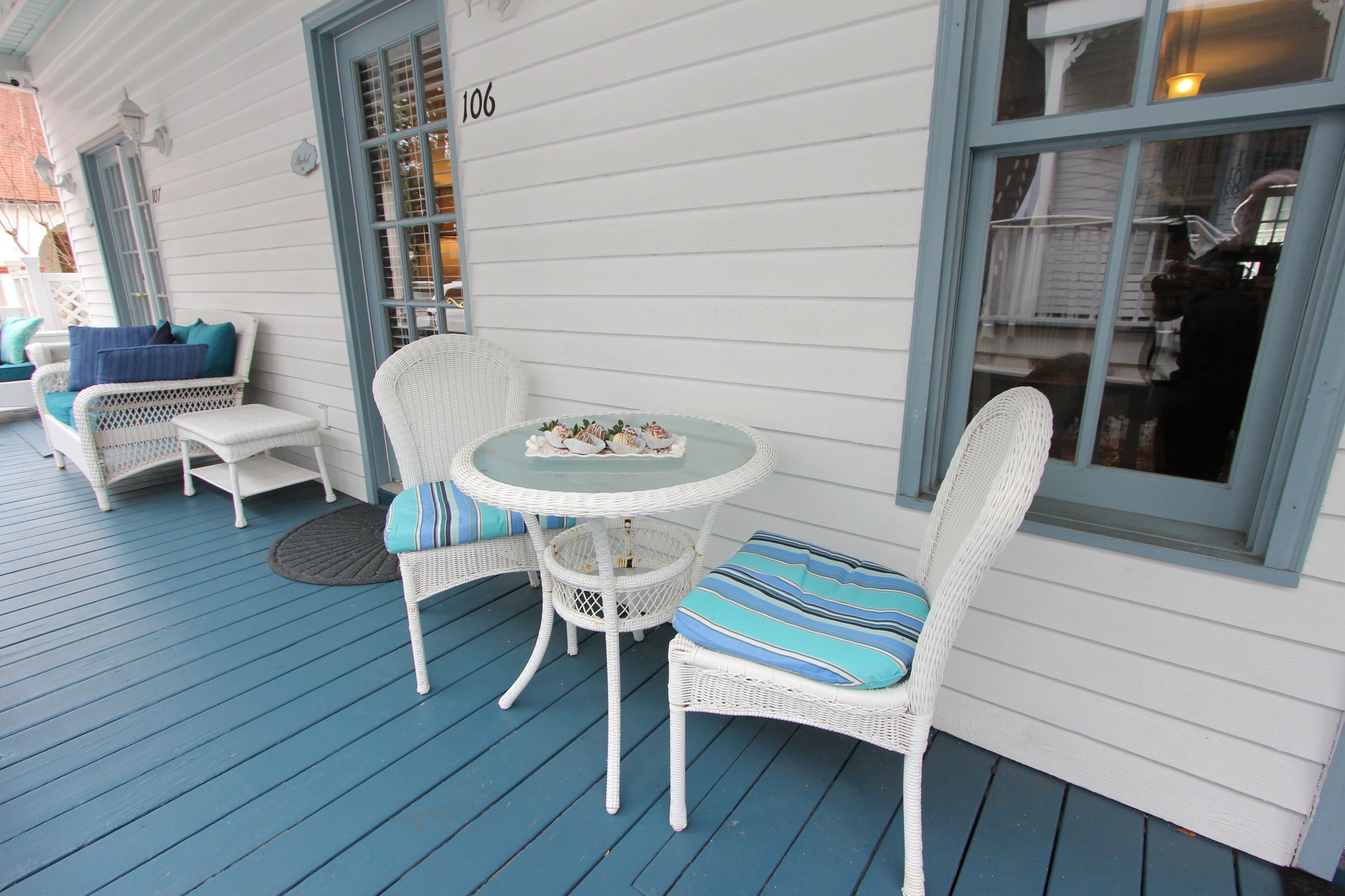 A porch with white wicker furniture, a round table, and a view of the street.