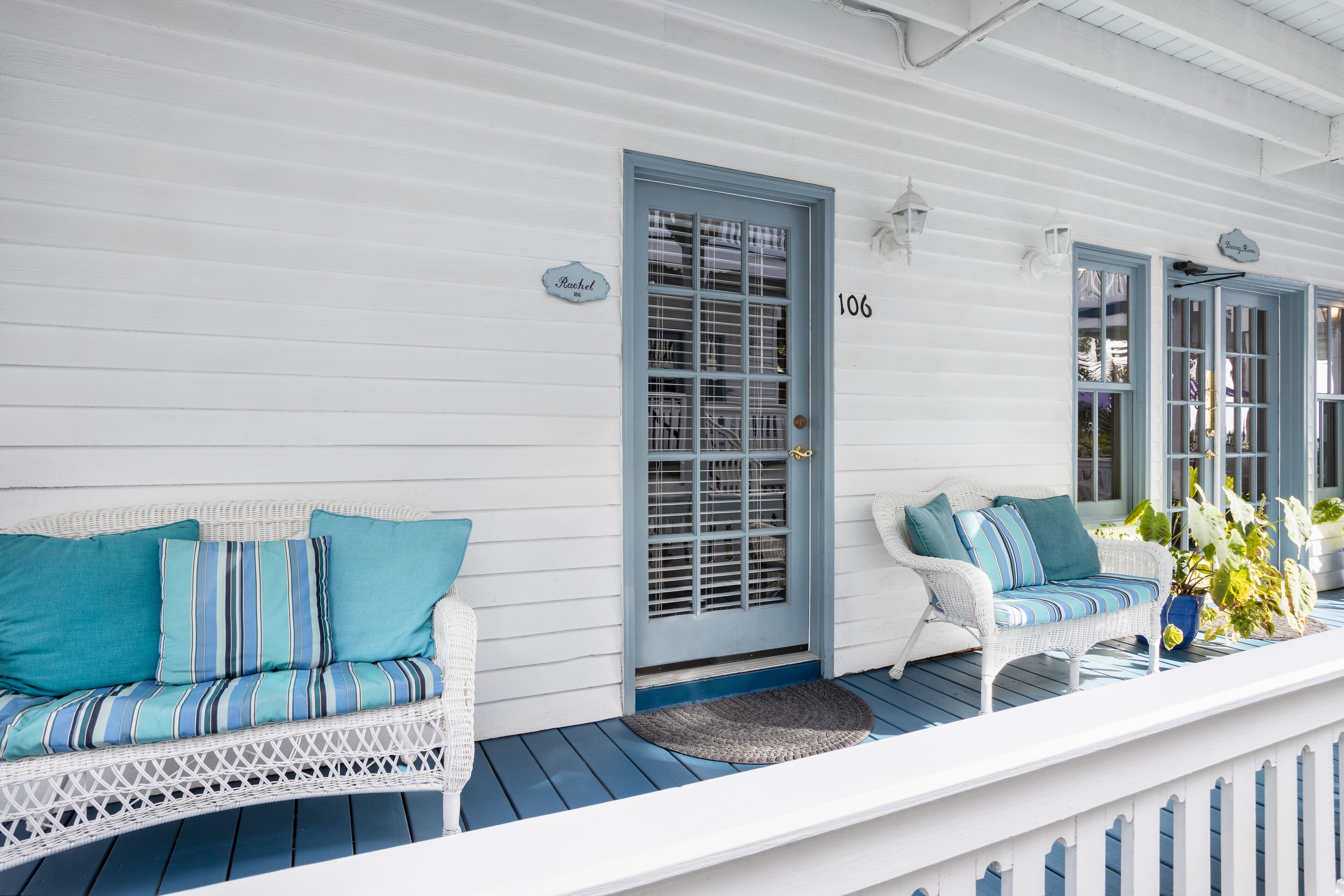 A porch with a white wicker sofa and a white chair, both with blue cushions.