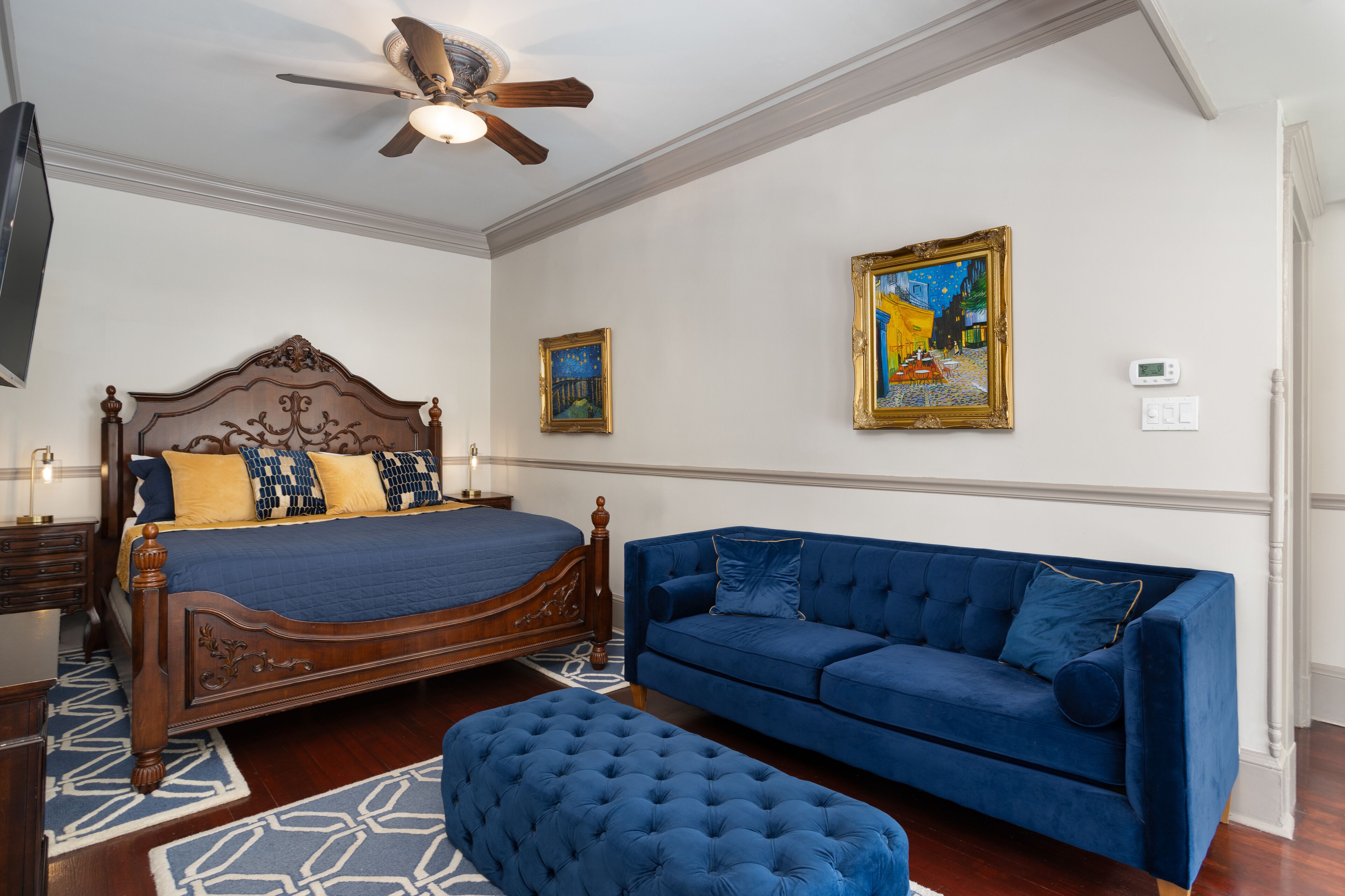 Un dormitorio con una cama de madera, un sofá azul y dos cuadros en la pared.