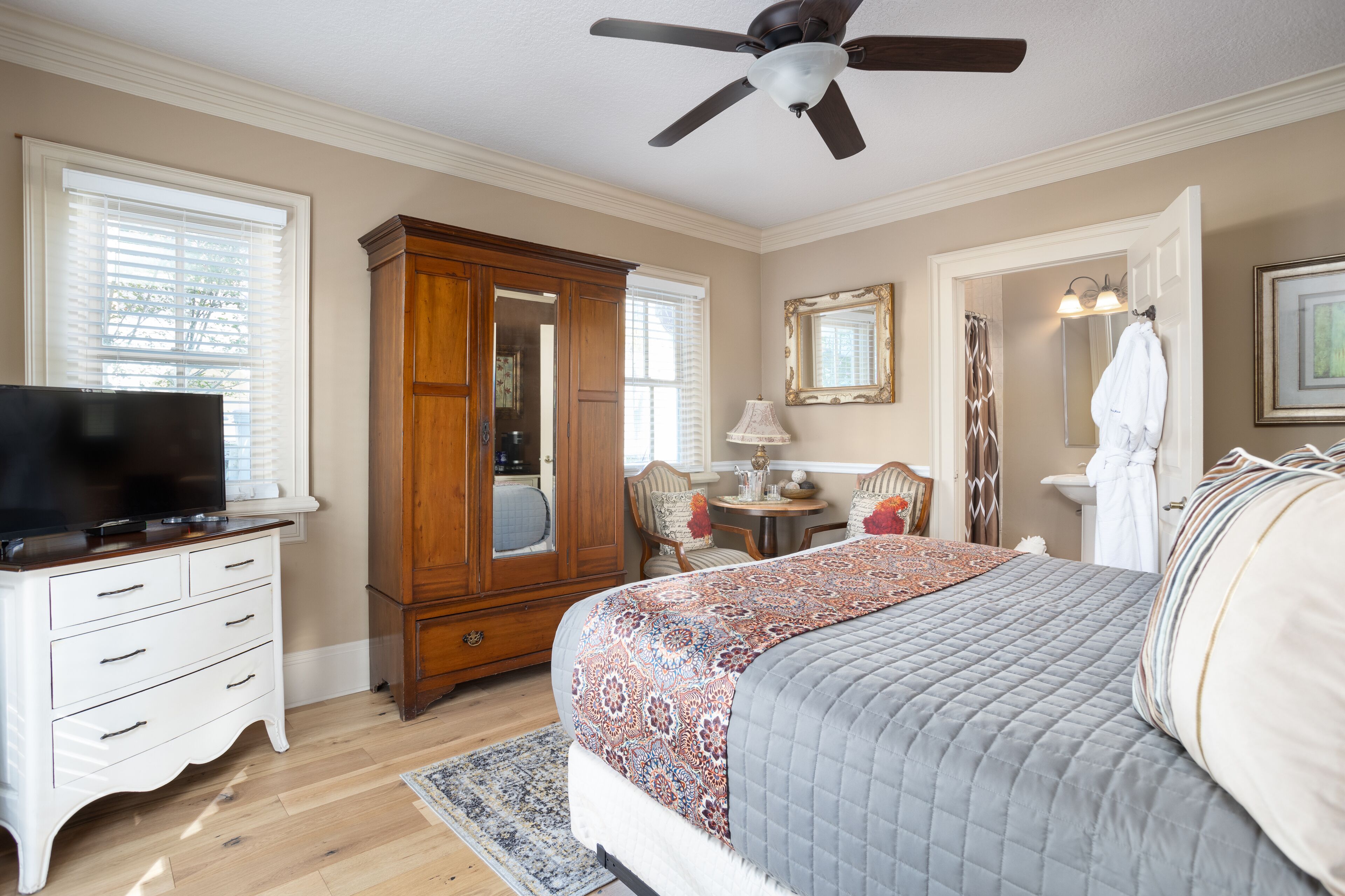 A bedroom with a bed, a wardrobe, a television, a ceiling fan, and a bathroom visible through an open door.