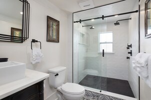 Un baño moderno con ducha de vidrio, inodoro blanco y lavamanos blanco.