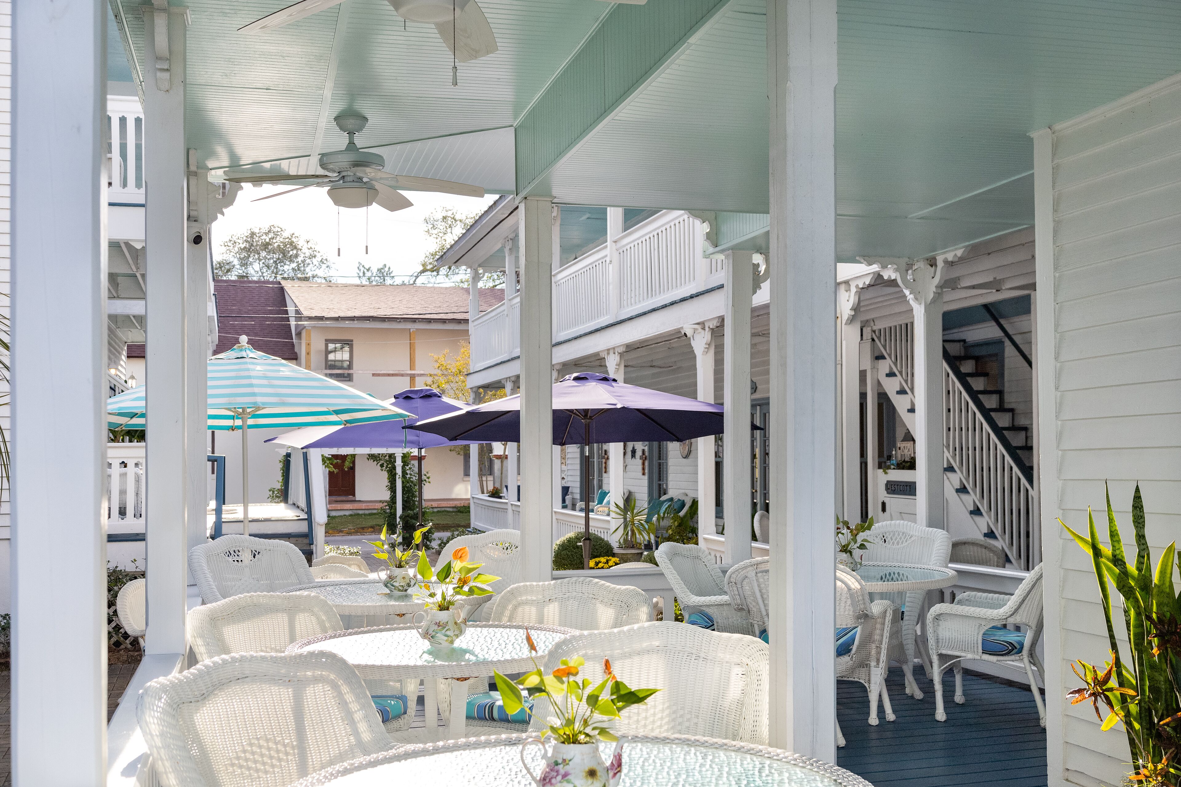 An outdoor patio with white wicker furniture, umbrellas, and potted plants.