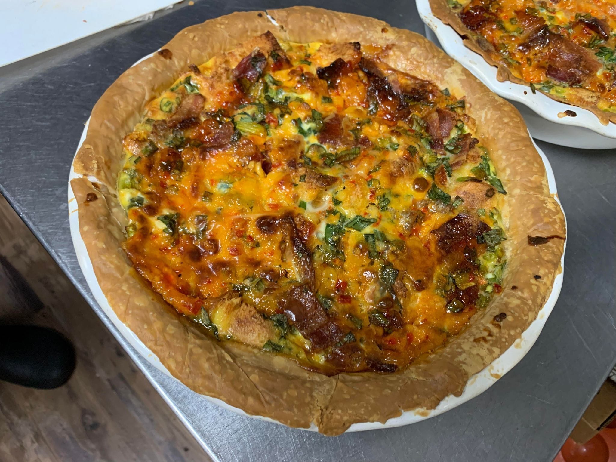 Une quiche à la croûte dorée, recouverte de fromage fondu et d’herbes fraîches, servie dans une assiette blanche.