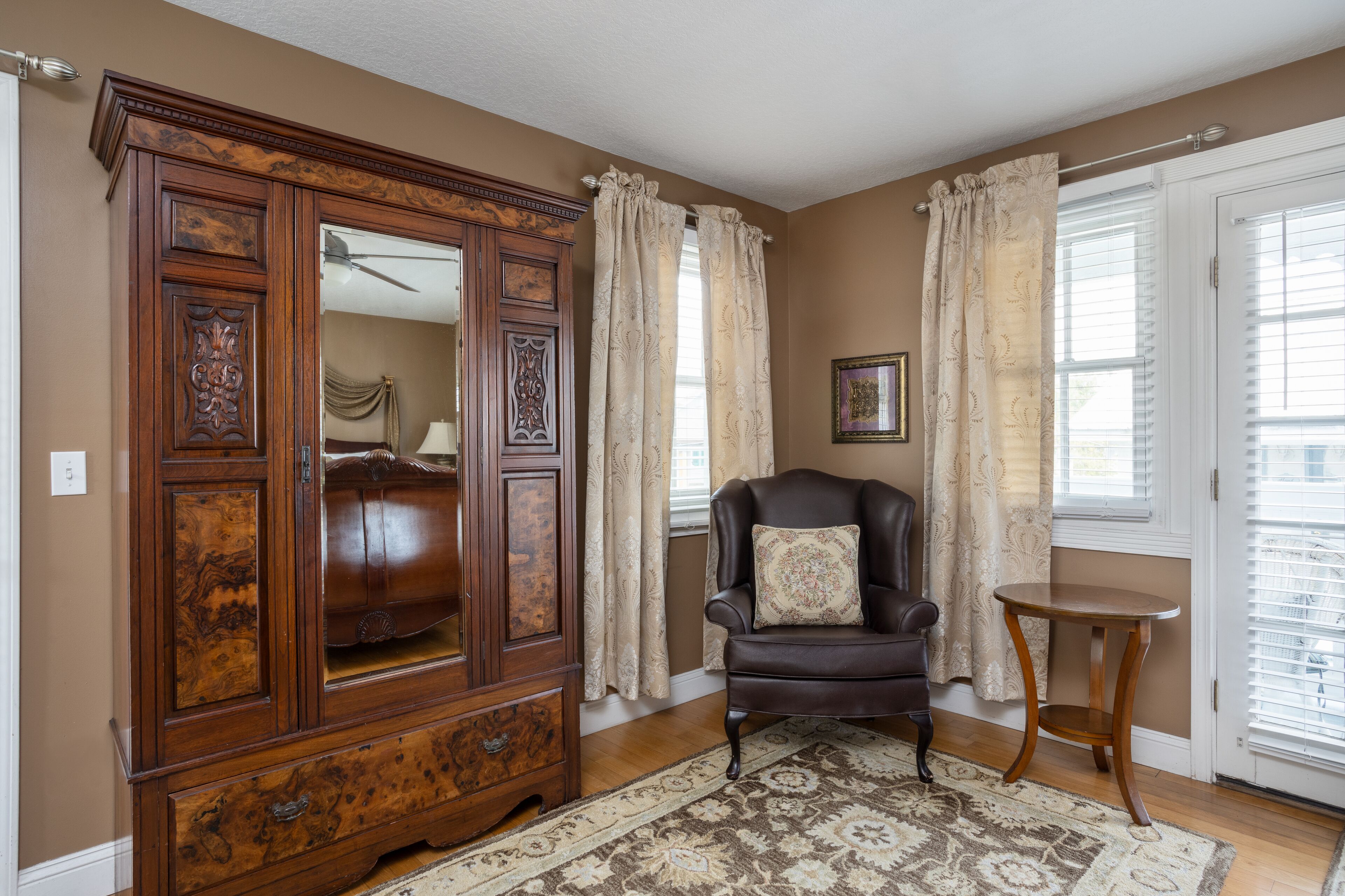 A room with a large wooden cabinet, a leather armchair, a small round table, and a patterned rug.