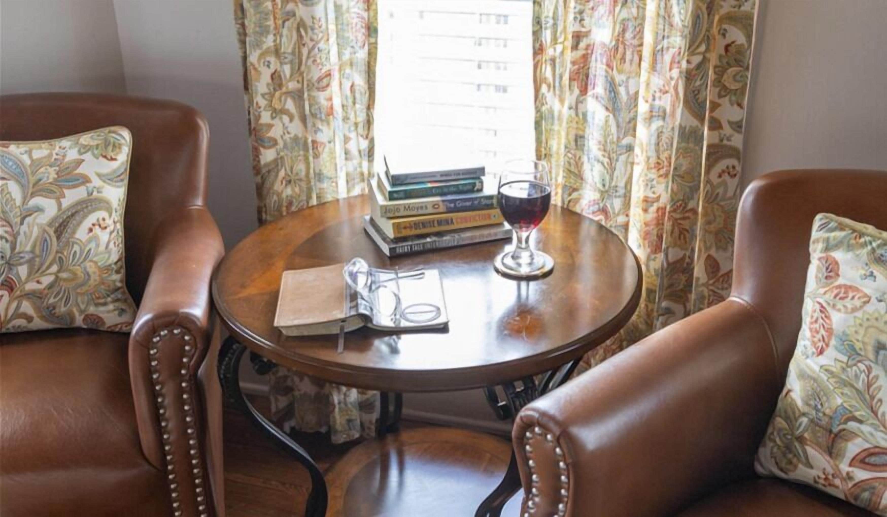 Una habitación con dos sillones de cuero, una mesita redonda con un libro, una copa de vino y un par de gafas.