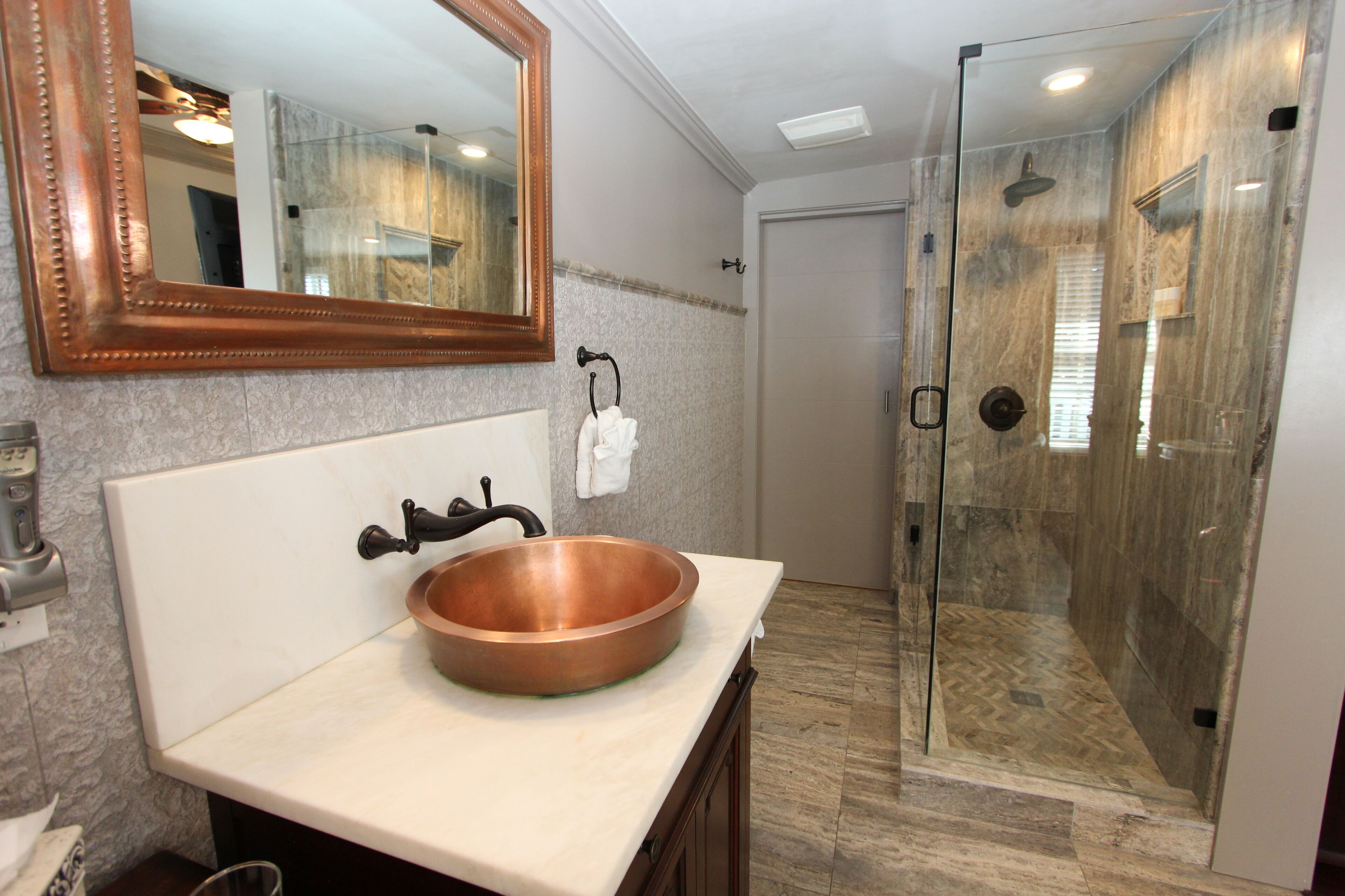 A bathroom with a copper sink, a large mirror, and a glass-enclosed shower.