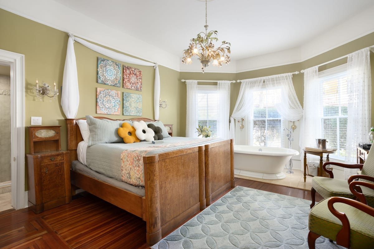 Un dormitorio con cama de madera, una araña, una bañera y obras de arte en las paredes.