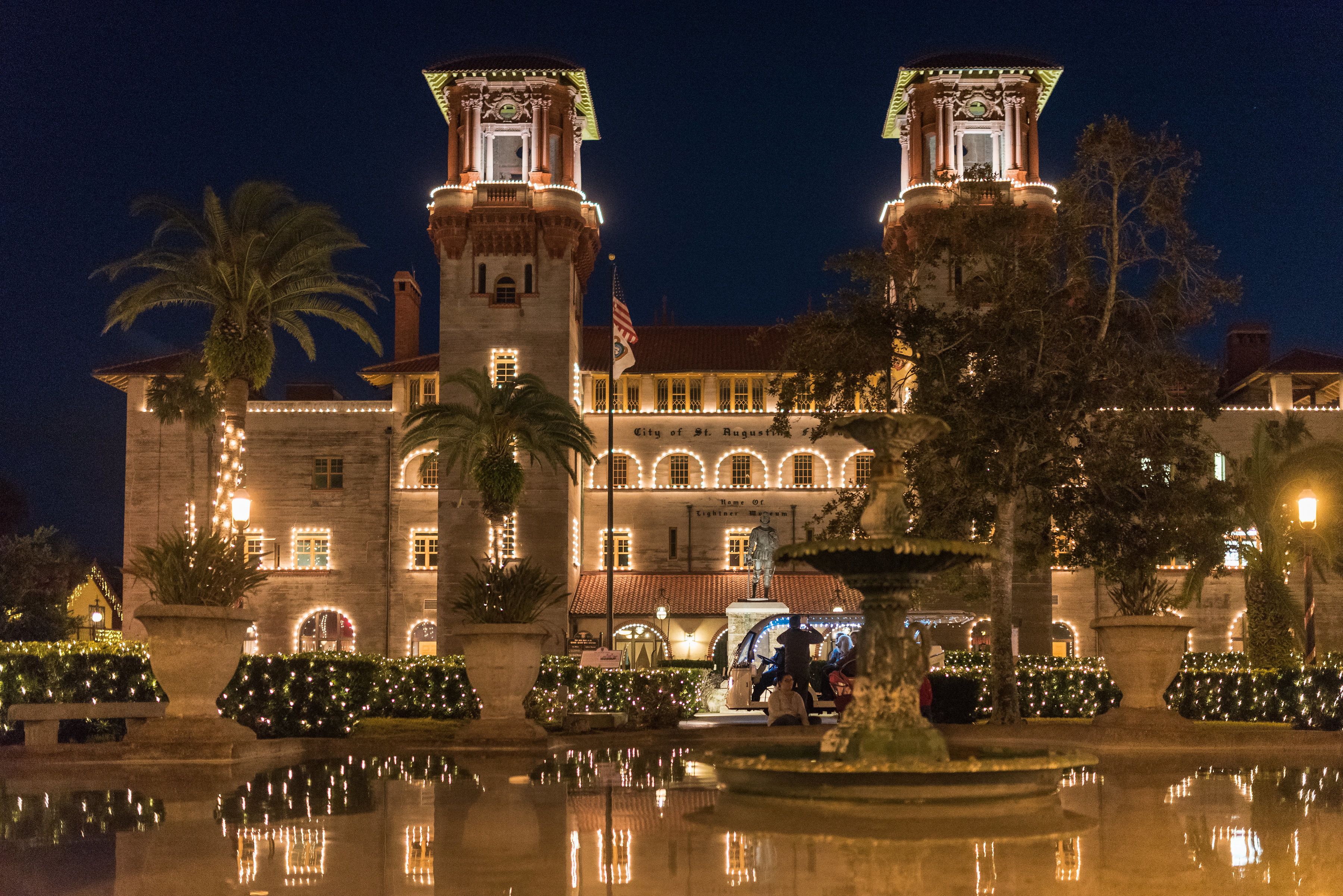 A historic building with two towers, a fountain, and a well-maintained garden.