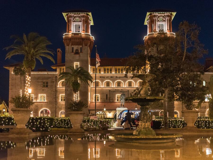 A historic building with two towers, a fountain, and a well-maintained garden.
