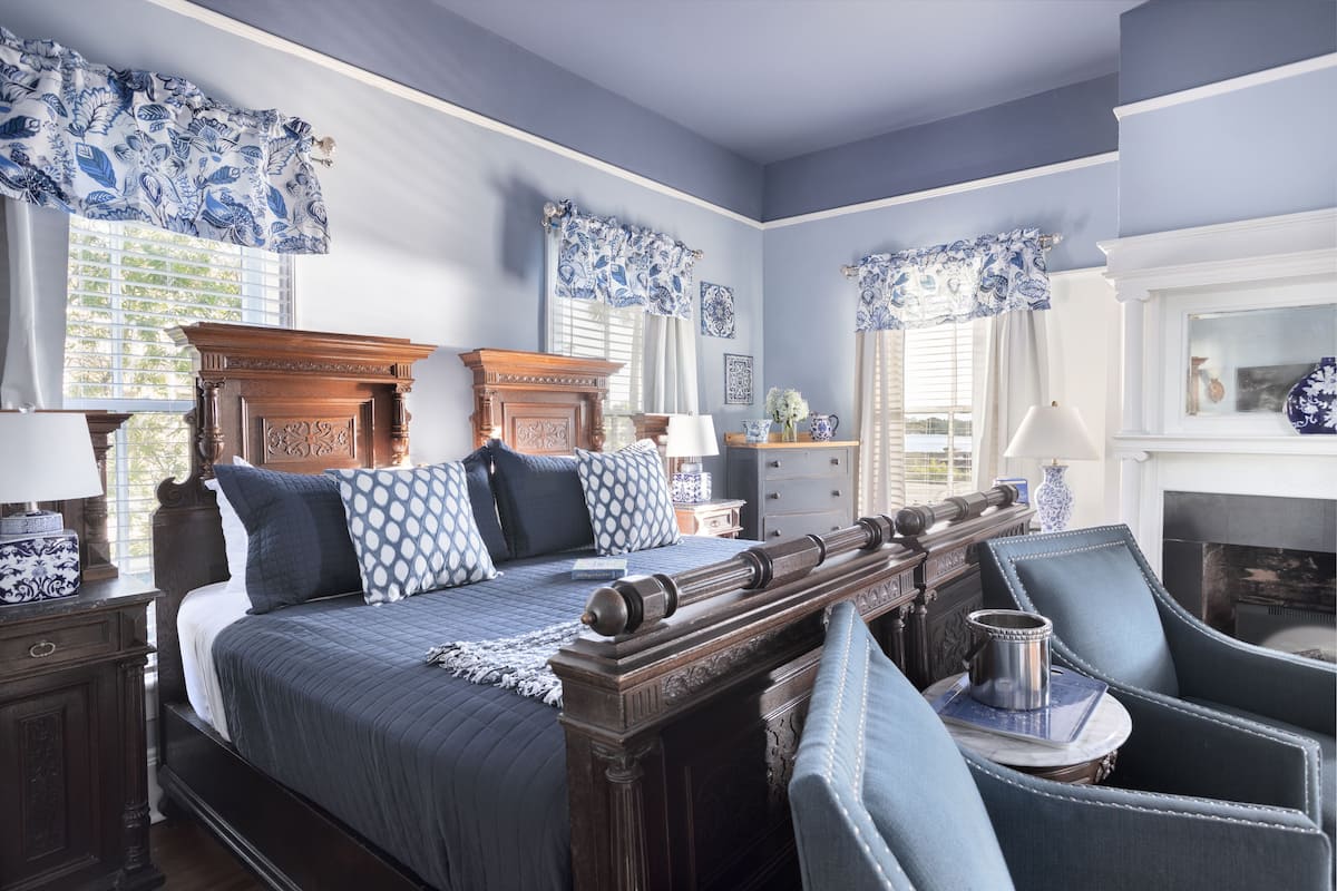 Un dormitorio con una cama grande, cabecera de madera y cortinas azules estampadas.