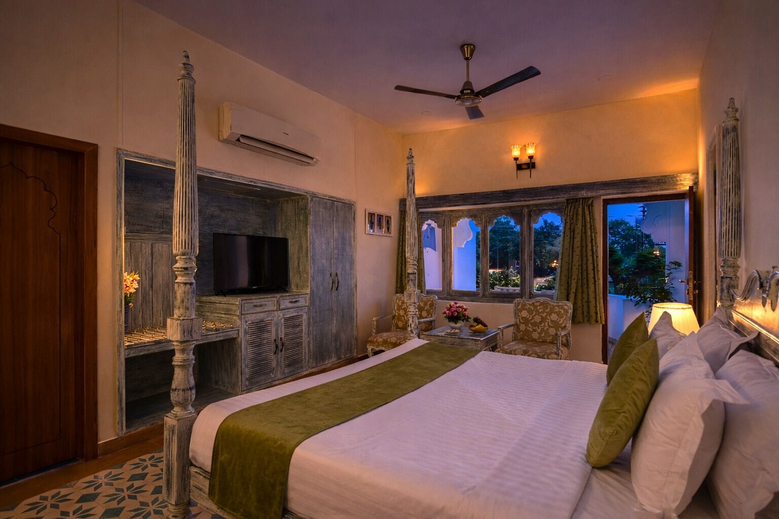 A bedroom with a large bed, a television, a desk, and a view of the outdoors.