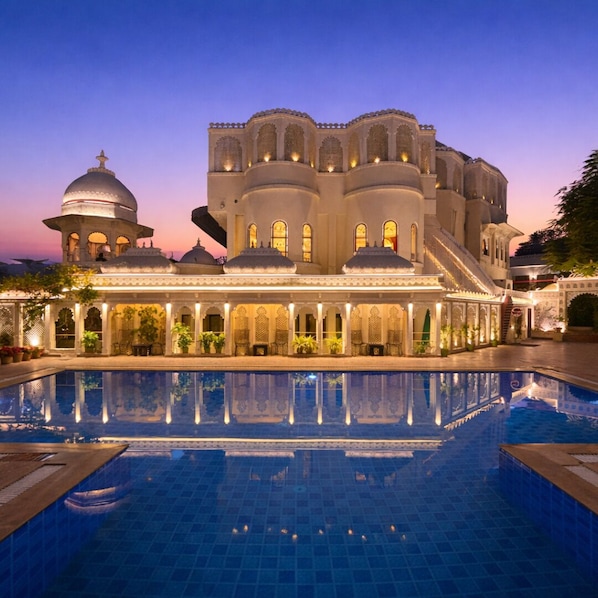 Un edificio grande con múltiples cúpulas y arcos, piscina e iluminación destacada en la fachada.