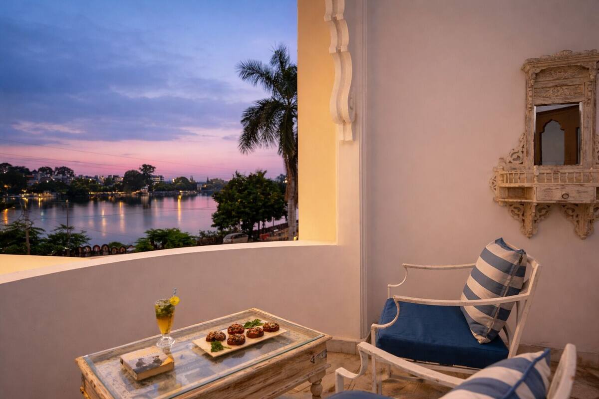 Un balcon donnant sur un lac, une table garnie de nourriture, une chaise avec un coussin et un miroir décoratif.