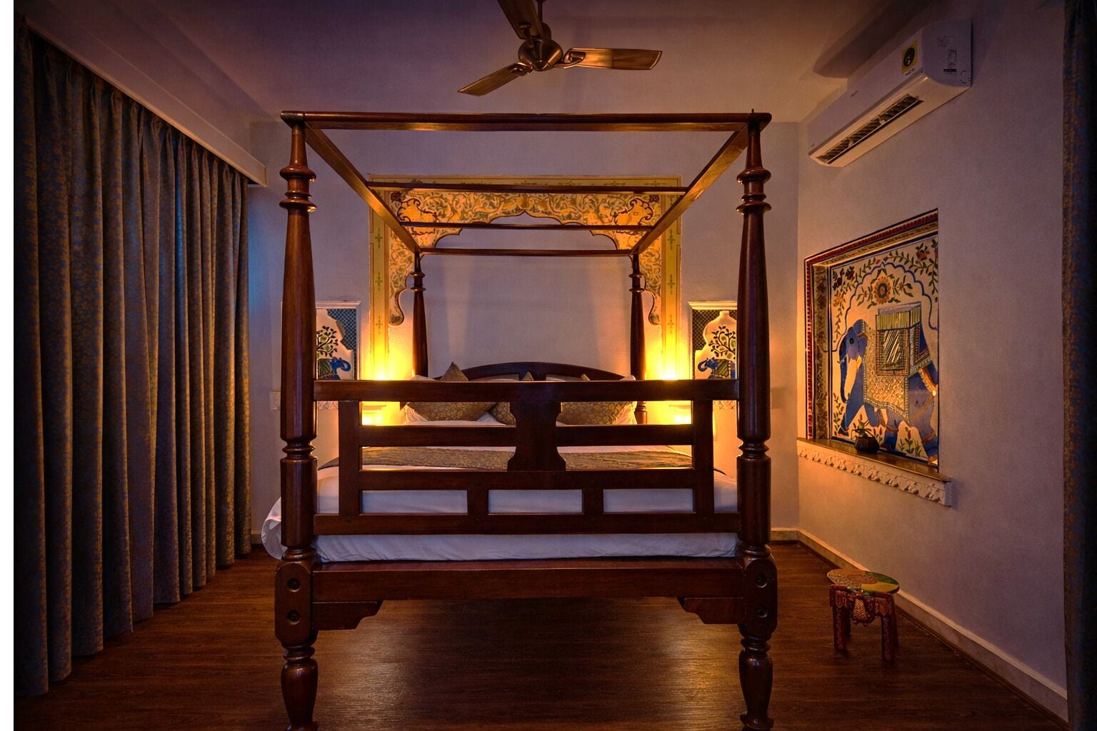 A four-poster bed with a ceiling fan, a painting on the wall, and a window with a view of the outside.