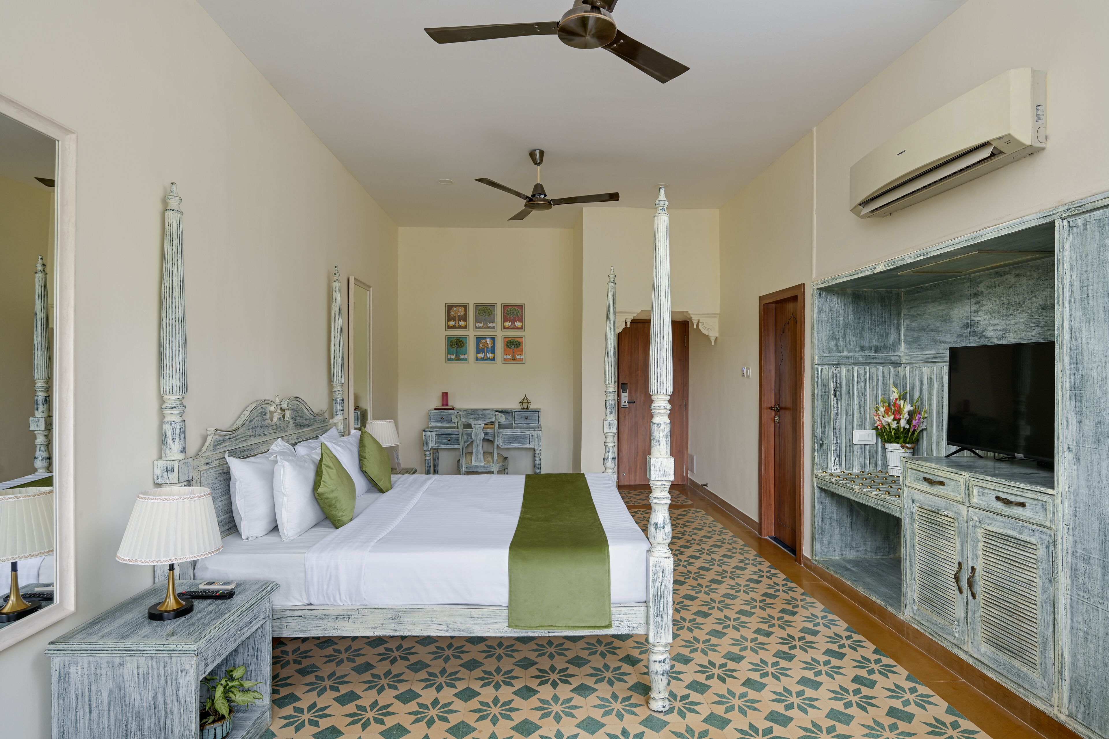 Un dormitorio con cama con dosel, ventilador de techo, televisor y un espejo decorativo.