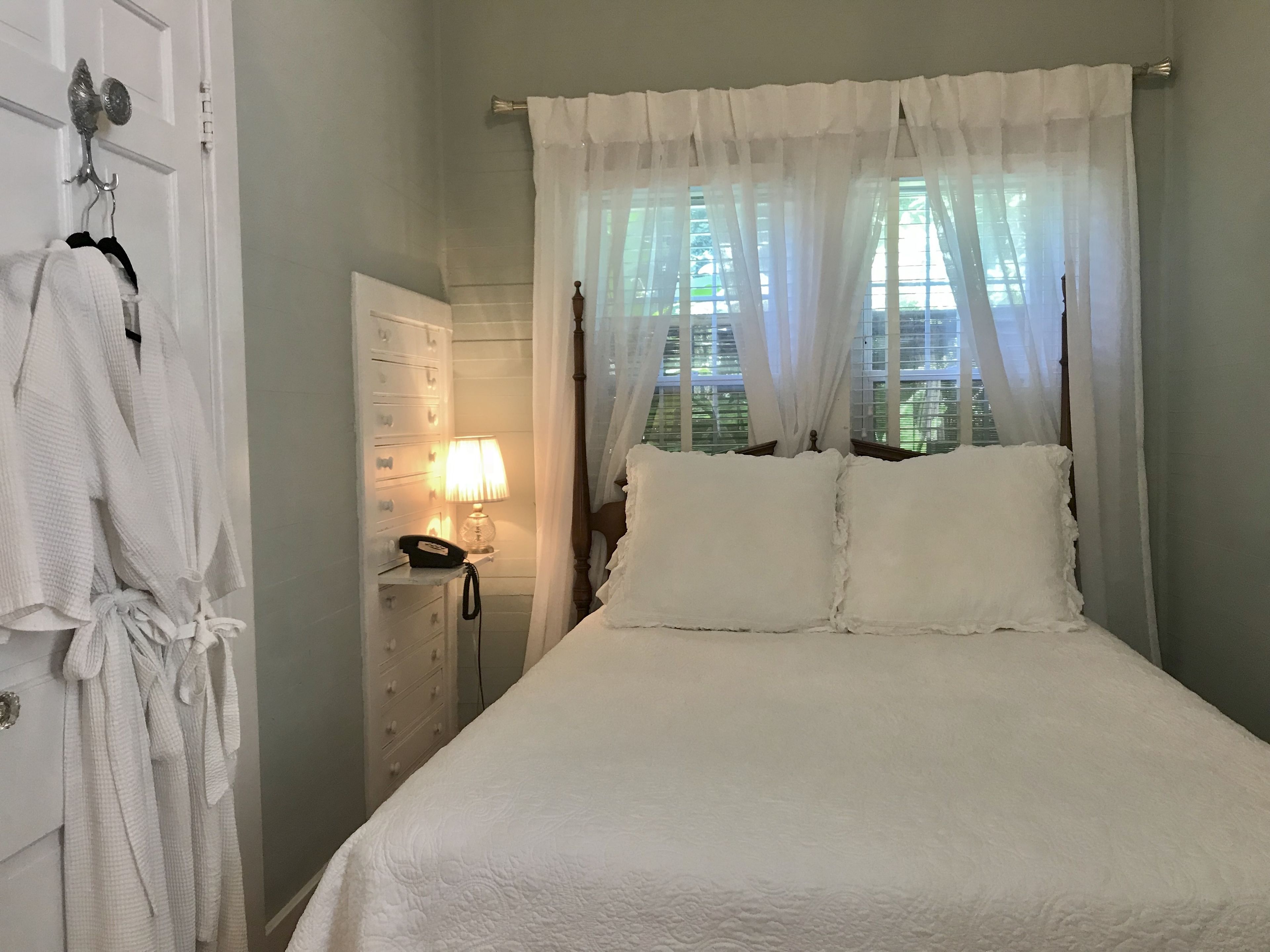 A neatly made bed with white linens, a bedside lamp, and a wooden headboard.