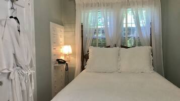 A neatly made bed with white linens, a bedside lamp, and a wooden headboard.