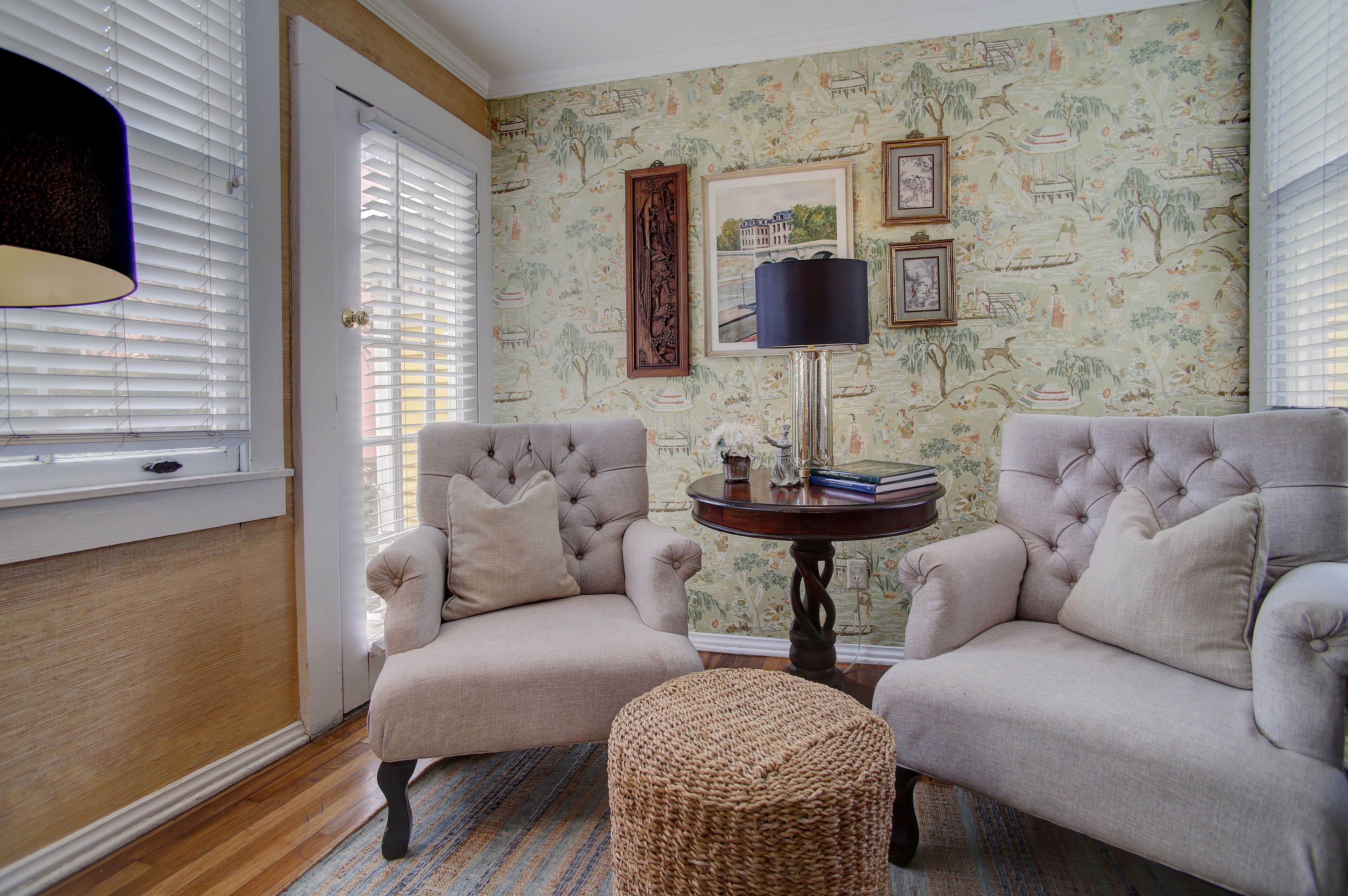 A room with two upholstered armchairs, a small round table with a lamp, and a patterned wallpaper.