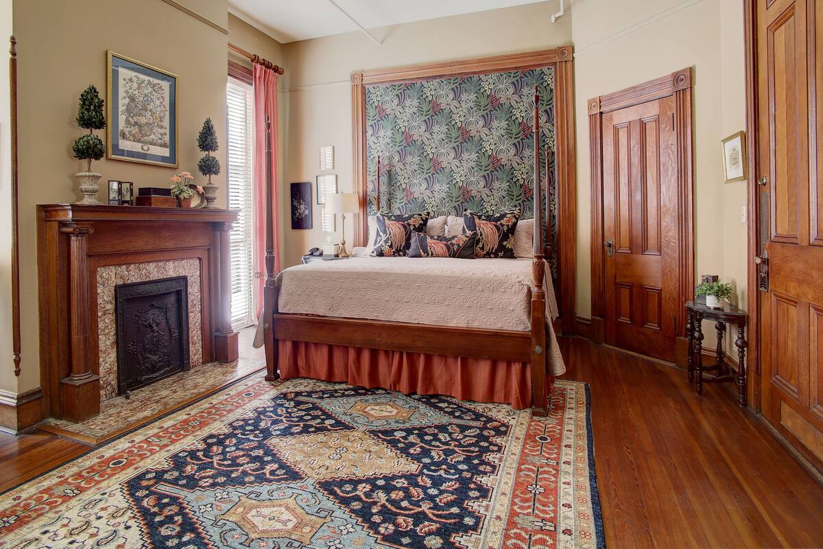 A traditional bedroom with a four-poster bed, a fireplace, and a large patterned tapestry.
