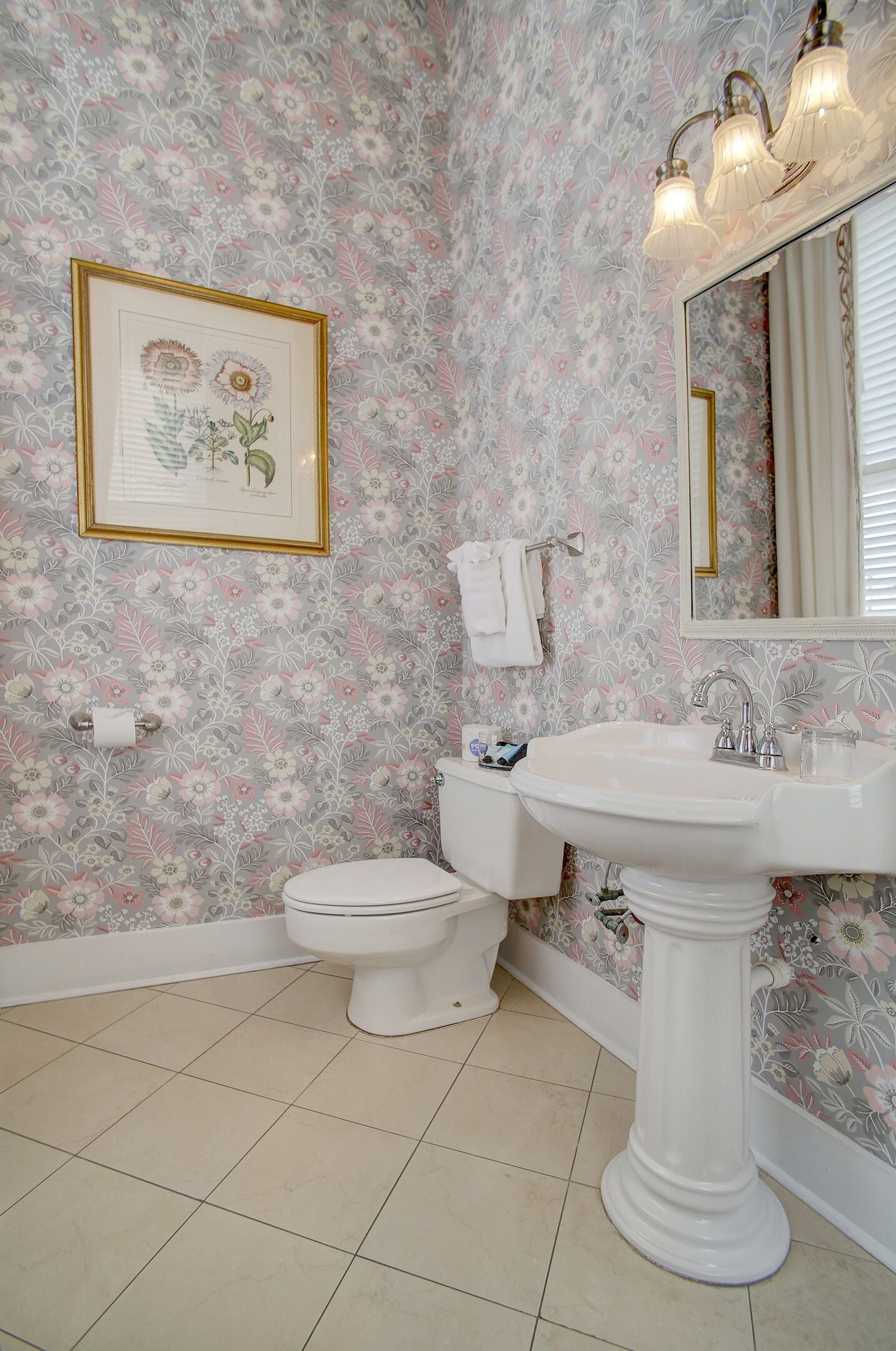 A bathroom with floral wallpaper, a pedestal sink, a toilet, and a framed botanical illustration.