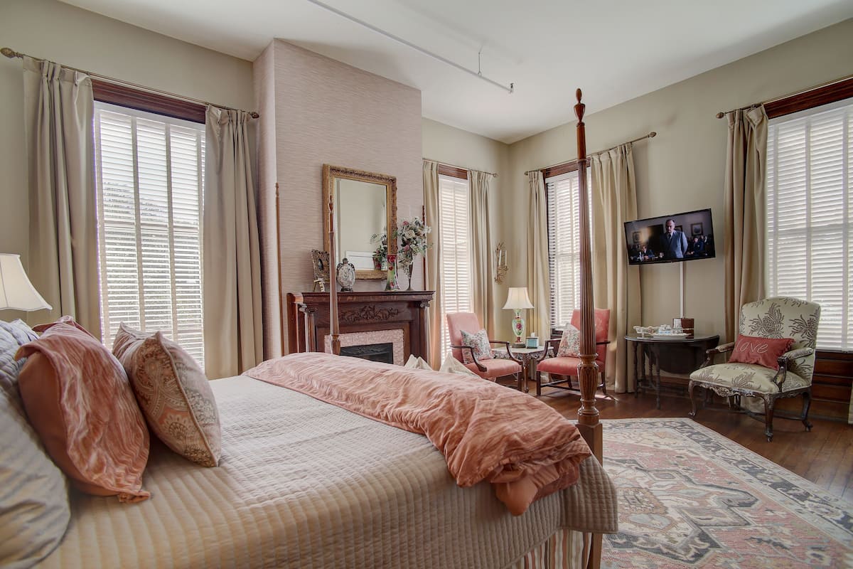 A spacious bedroom with a large bed, a fireplace, a television, and multiple seating areas.