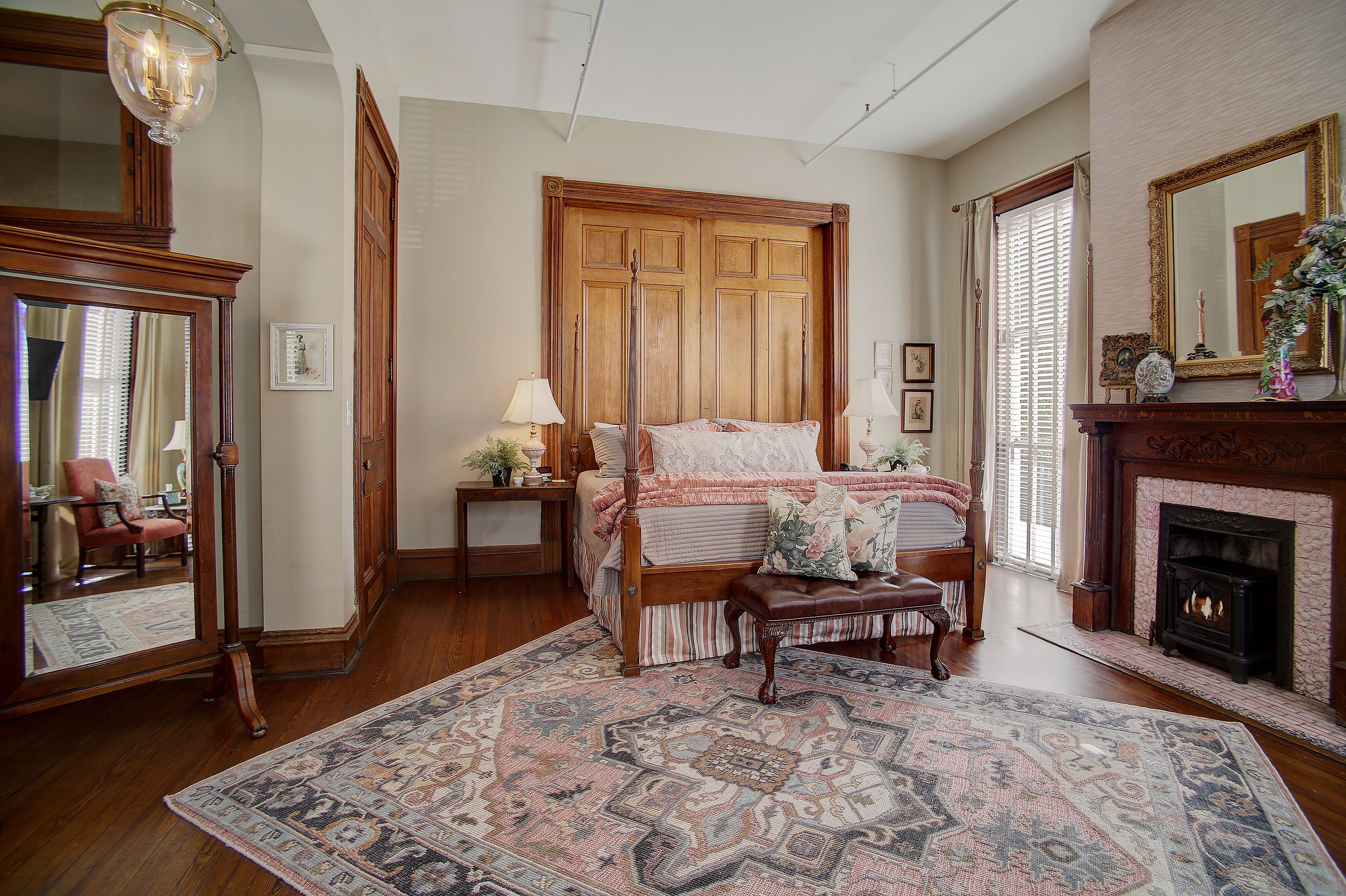 A traditional bedroom with a large bed, a fireplace, and a mirror.