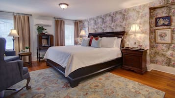 A neatly arranged bedroom with a large bed, a chair, a nightstand, and a wall with floral wallpaper.