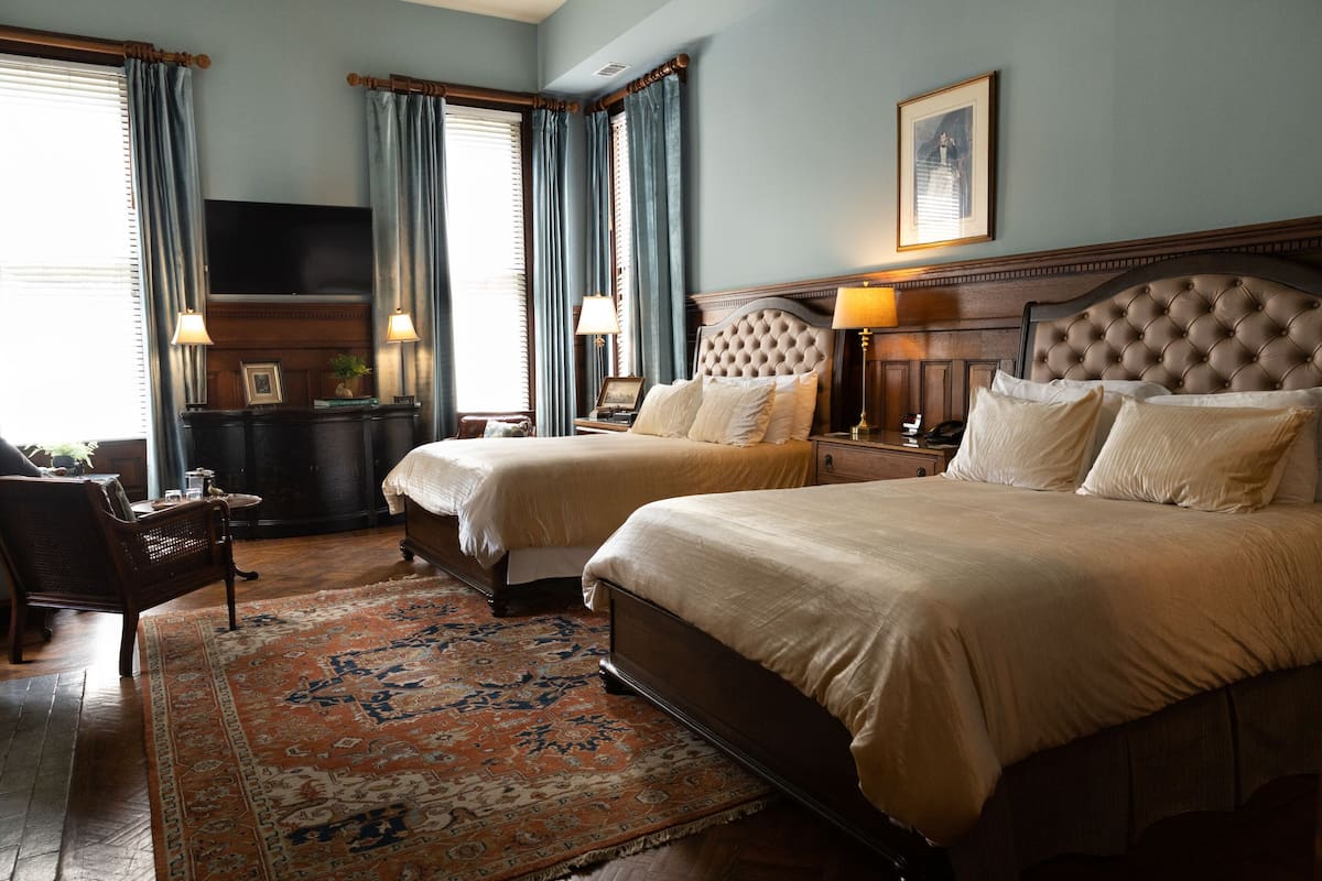 A hotel room with two beds, a large rug, a television, and a framed picture on the wall.