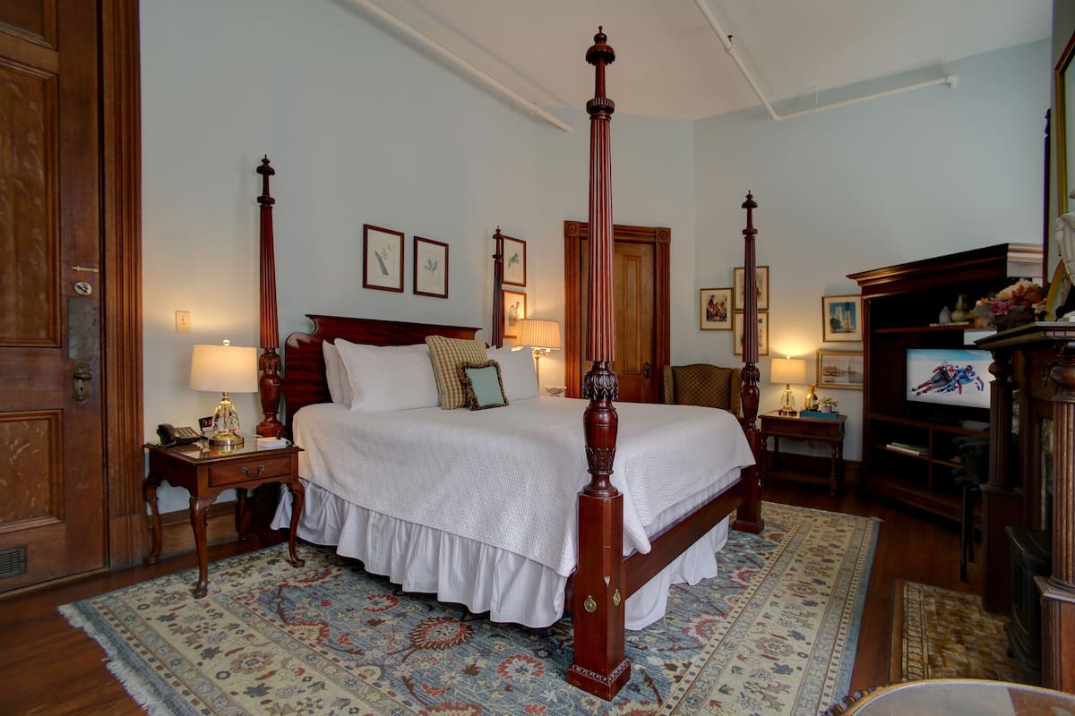 A four-poster bed with a wooden canopy, a nightstand with a lamp, a wooden dresser, and a television on a wooden stand.