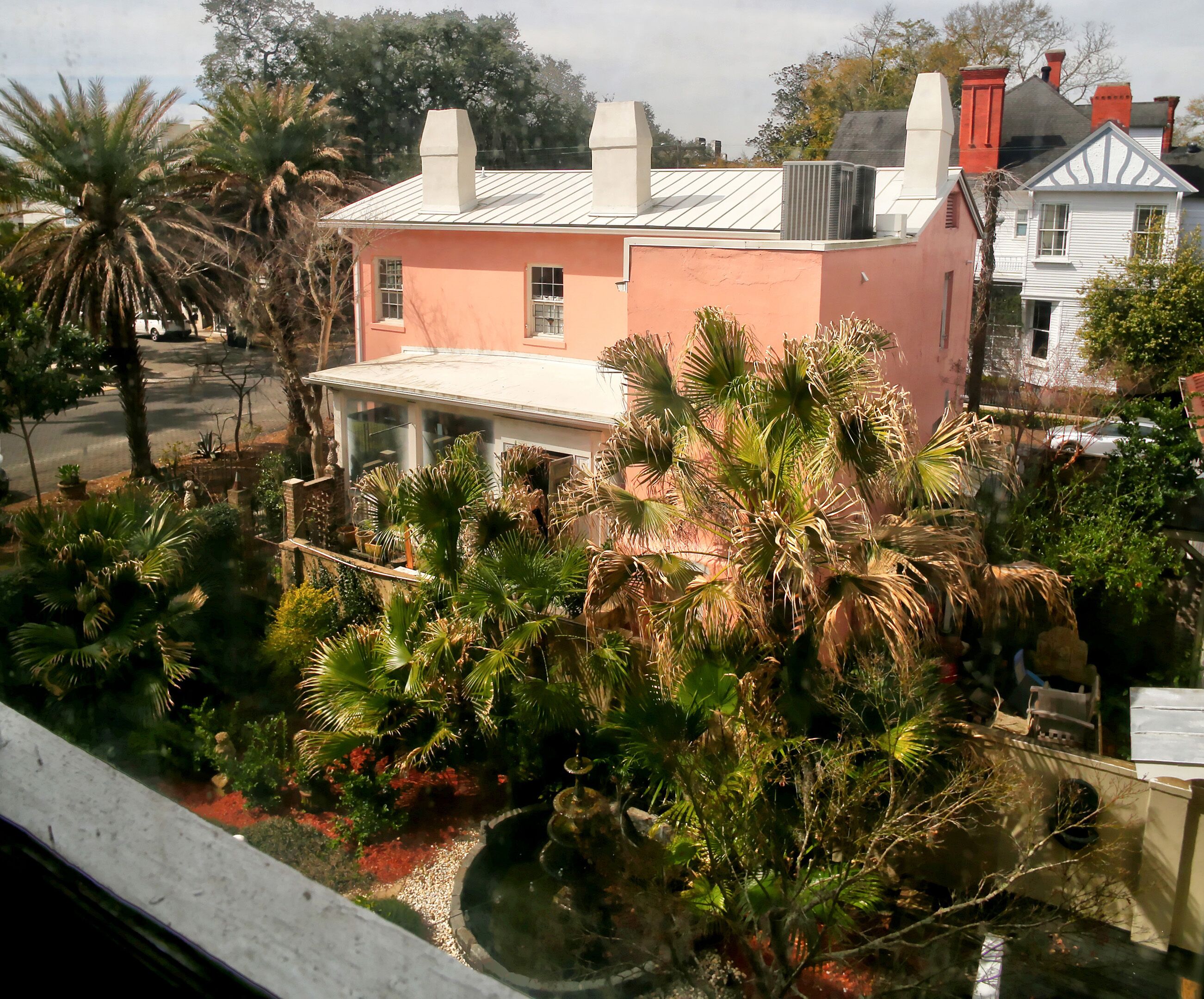 A pink house with a white porch, surrounded by palm trees and a small pond.
