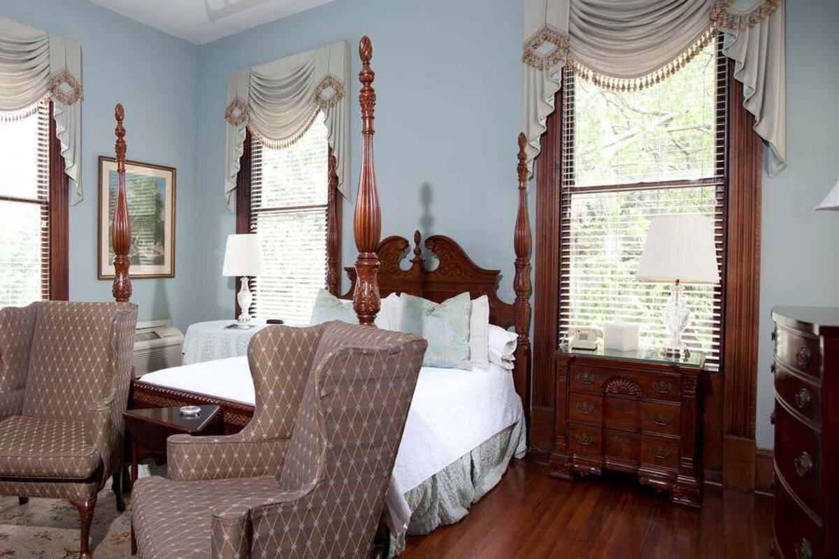 A bedroom with a large bed, two armchairs, a nightstand, a dresser, and a potted plant.
