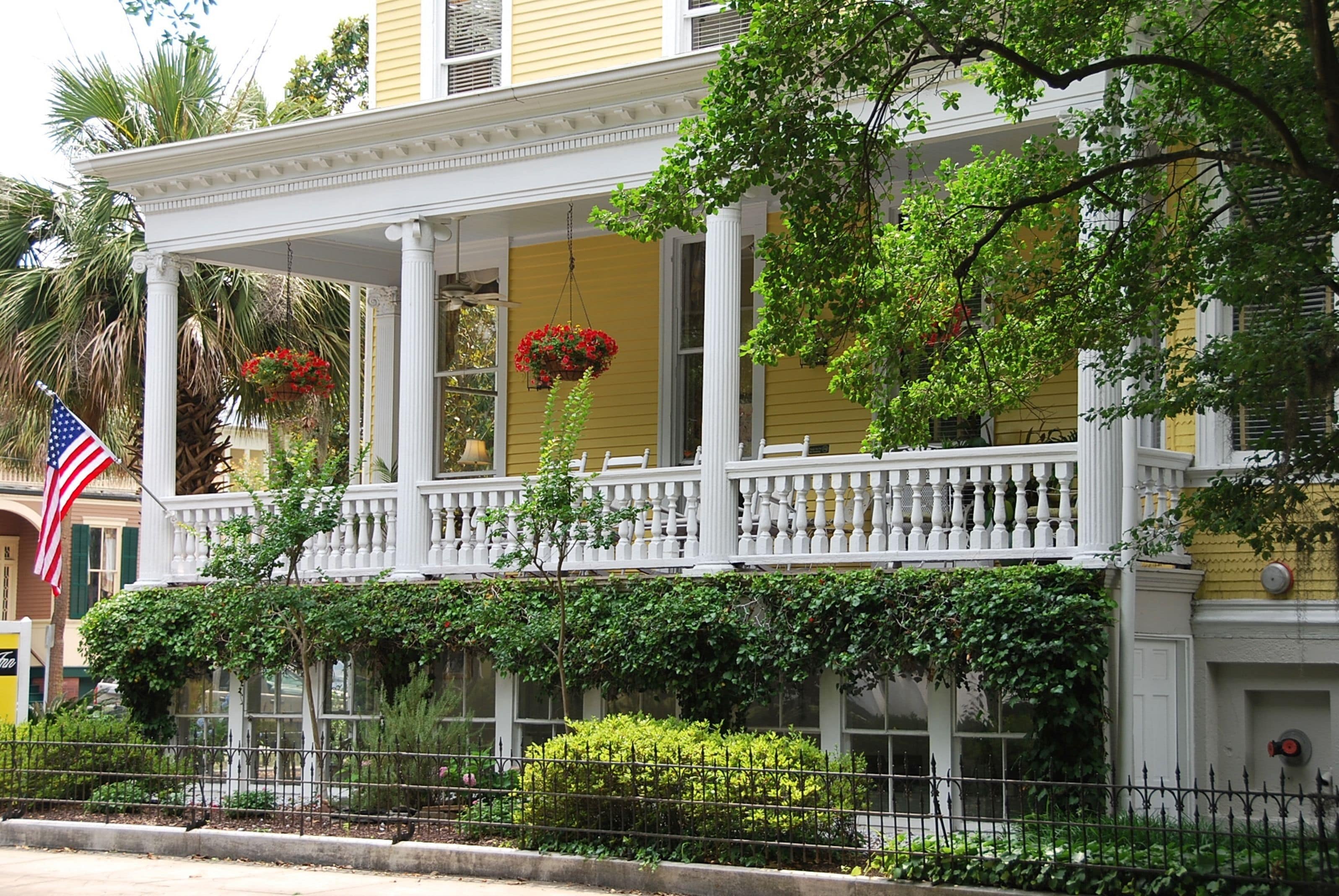A yellow building with a white porch, red flowers, and an American flag.