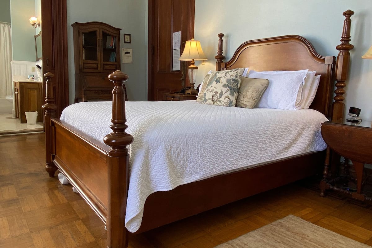 A wooden four-poster bed with white bedding, two bedside lamps, and a nightstand with a clock.