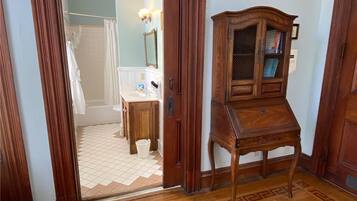 A wooden cabinet with a glass door, a bathroom with a white bathtub, and a tiled floor.
