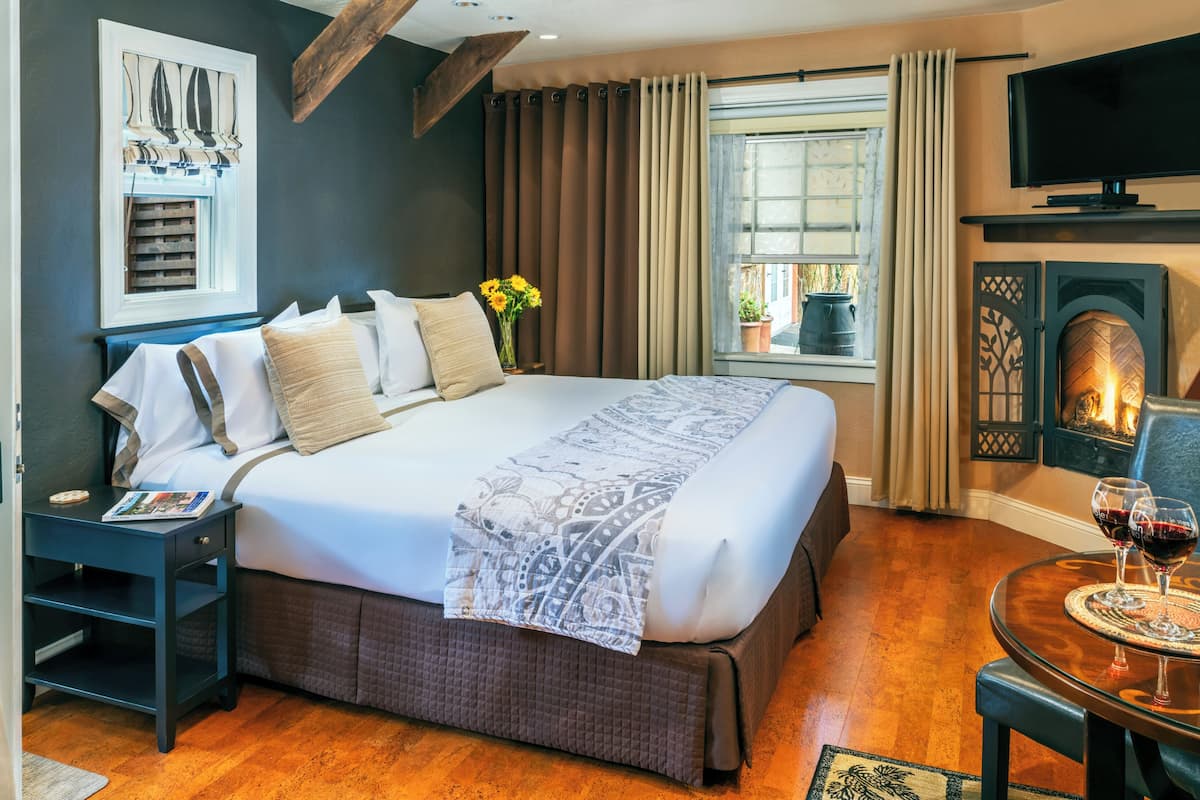 A hotel room with a large bed, a television, a fireplace, and a window with curtains.