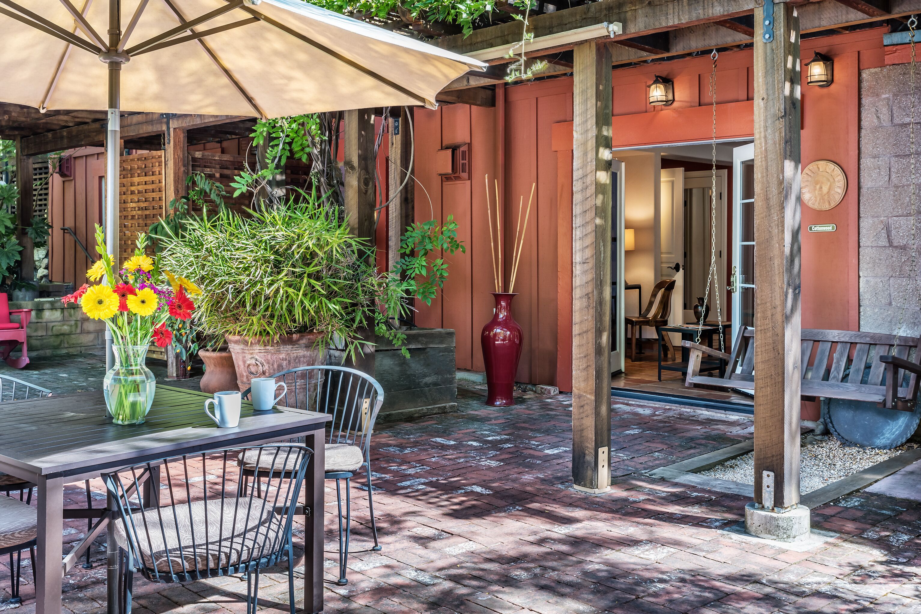 Un patio al aire libre con una mesa, sillas, un paraguas grande y macetas con plantas.