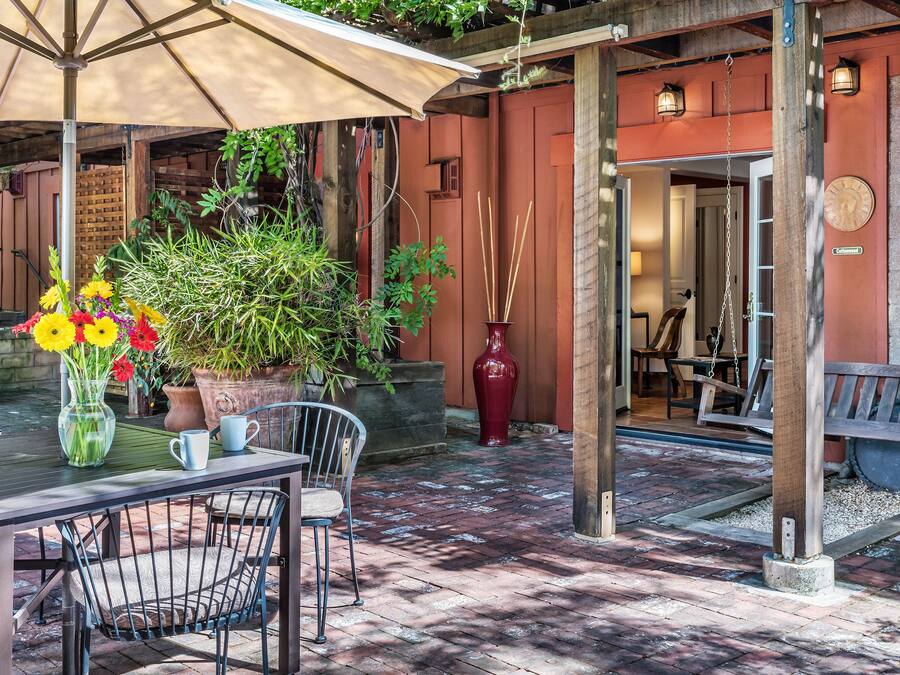 Un patio al aire libre con una mesa, sillas, un paraguas grande y macetas con plantas.